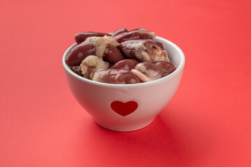 Raw Chicken Hearts in Heart-Decorated Bowl on Red Background Highlighting Culinary Concepts