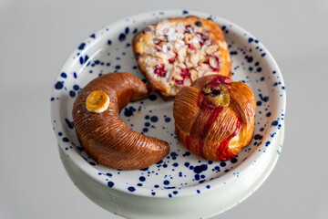 Plate with artisanal pastries including a banana-shaped banana cake, a fruity muesli cheesecake pastry, and a pistachio-filled pastry, perfect for breakfast or coffee break.