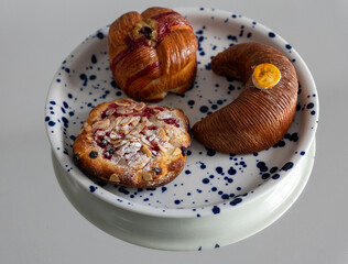 Plate with artisanal pastries including a banana-shaped banana cake, a fruity muesli cheesecake pastry, and a pistachio-filled pastry, perfect for breakfast or coffee break.