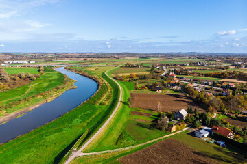 Wide aerial drone view of the Vistula River (Wisła) near Ispina village, Krakow area, Poland. Scenic landscape featuring flood embankments, rural houses, and a cycling route.