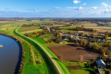 Wide aerial drone view of the Vistula River (Wisła) near Ispina village, Krakow area, Poland. Scenic landscape featuring flood embankments, rural houses, and a cycling route.