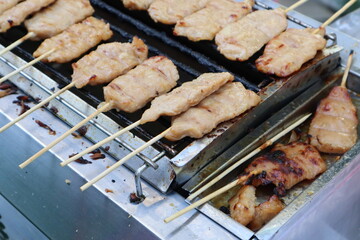 Skewered pieces of marinated pork (Moo Ping) are grilling on a small metal charcoal grill.