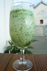 Thick green vegetable smoothie mixed with yogurt in wine glass on wooden table outdoors. Represents healthy beverage choice, wellness lifestyle habit, probiotic nutrition, and clean eating refreshment