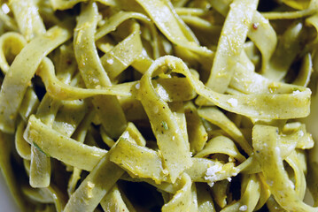 Green tagliatelle pasta ribbons tossed with herbs and parmesan cheese in close-up macro view. Represents homemade pasta creation, Italian culinary art, herb-infused noodles, and Mediterranean cooking.