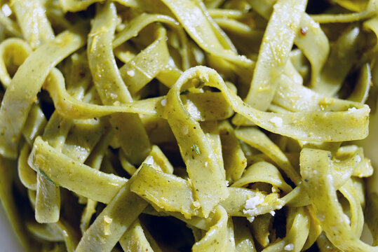 Green tagliatelle pasta ribbons tossed with herbs and parmesan cheese in close-up macro view. Represents homemade pasta creation, Italian culinary art, herb-infused noodles, and Mediterranean cooking.