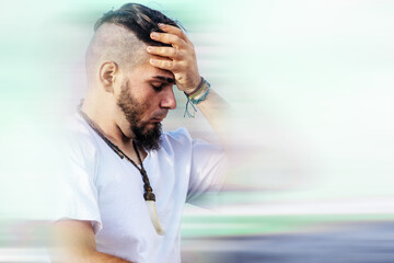 Young adult male with distressed expression holding forehead in motion-blurred background,