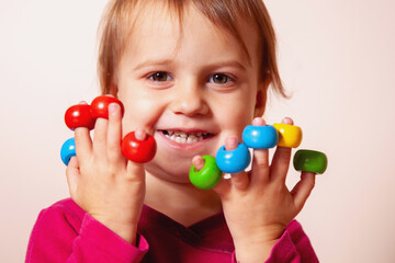 Smiling child playing with colorful wooden toys on her fingers.