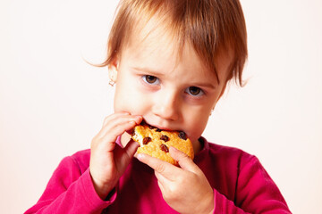 Child with crumbs on her face holding a snack in the studio.