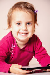 Little girl looking at the camera with a cheerful smile and a tablet.