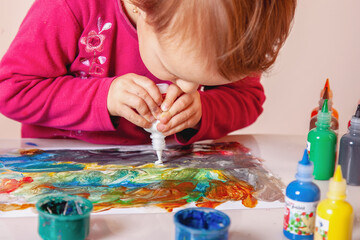 Child concentrating on creating artwork using colorful paints and glue.