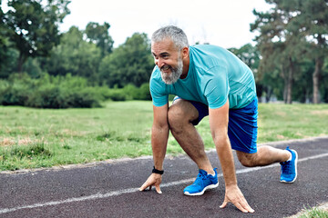 Smiling active mid aged man standing in start position,  jogging running and walking doing fitness in the park