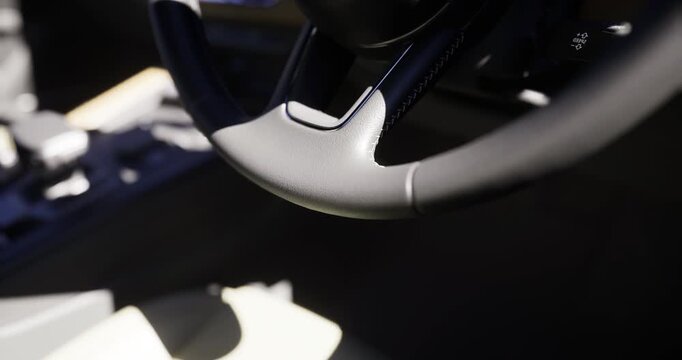 A close up view captures the sleek design of a modern car steering wheel set against a stylish and minimalistic interior. Sunlight highlights the contours and materials used.