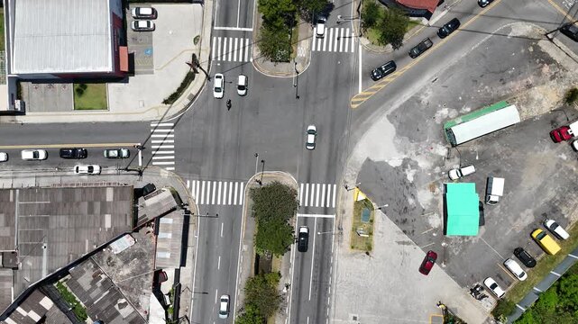 Vis&atilde;o a&eacute;rea de cruzamento movimentado com ve&iacute;culos em diferentes dire&ccedil;&otilde;es, mostrando infraestrutura vi&aacute;ria, circula&ccedil;&atilde;o intensa e organiza&ccedil;&atilde;o do tr&aacute;fego em &aacute;rea urbana consolidada.