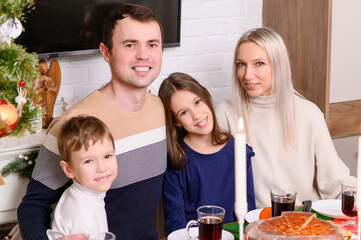 Portrait of happy family at Christmas table. Parents and children smile joyfully as they pose, celebrating holiday. Christmas Eve, family togetherness.