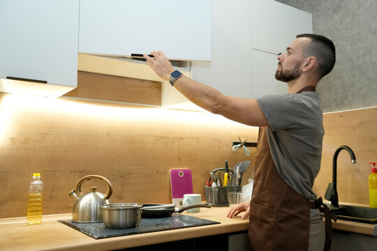 A focused man in an apron reaches for kitchen items while cooking dinner in a stylish kitchen. Pots, pans, and fresh vegetables are visible in this warm setting - Powered by Adobe