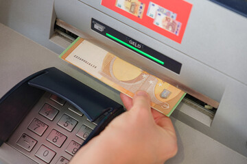 Hand withdrawing euro banknote from an ATM machine in Germany