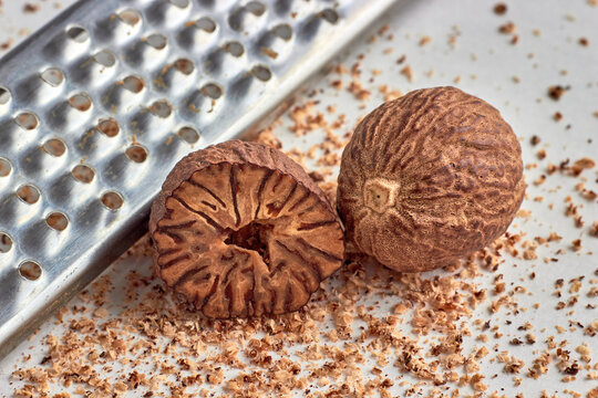 two nutmegs grated on a metal grater on a wooden table.