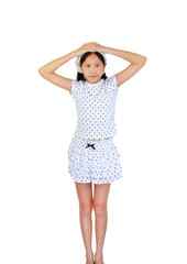 Portrait young Asian girl wearing white polka dot set stands with her hands clasped on her head against white background, looking directly at camera.