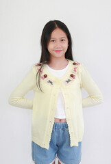 Happy young Asian girl standing against white background, casually posing in pastel yellow cardigan...