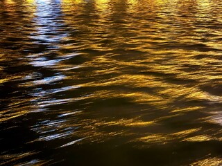 Dark river water surface with golden light reflections at night.