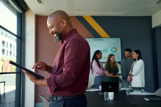 Smiling black mature businessman using tablet in office with colleagues in background