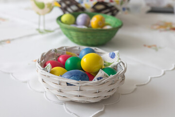A small woven basket full of brightly colored Easter eggs in blue, yellow, green and red. The basket is placed on a light, slightly blurred background