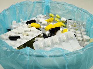Various expired pills and expired pill blister packs are  in  a container for disposal, side view. 