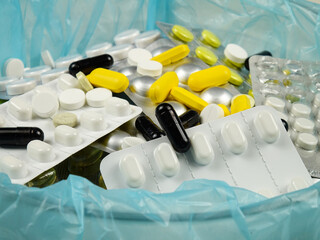 Various expired pills and expired pill blister packs are  in  a container for disposal, side view. 