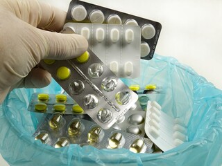 A hand in a white rubber glove puts  expired pill blister packs  into a container for disposal 