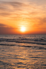 Obraz premium Sunset over the Baltic Sea with warm orange sky, gentle waves and a distant sailboat. Calm and serene seascape.
