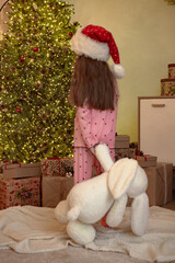 Cute child with soft toy looking at Christmas tree, focus on decorated tree with lights and garlands, Christmas Eve