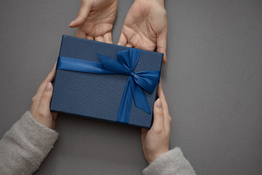 Top view of male and female hands holding blue gift box with ribbon on gray background Flat lay. Present for birthday, valentine day, Christmas, New Year, copy space