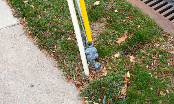 Utility pole guy wire anchor grounding point with yellow safety casing and metal tension hardware next to sidewalk.