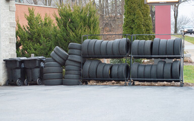 Exterior of an auto repair shop displaying racks of new tires and stacks of used tires on the pavement