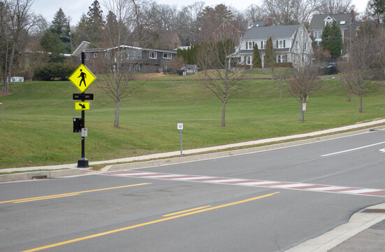 Wide angle view of a suburban pedestrian crosswalk with red and white striped road markings and a solar-powered flashing yellow warning sign