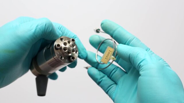 A scientist in blue gloves installs a 100 &micro;L sample loop onto a manual HPLC injector valve. Close-up of component assembly for liquid chromatography in a science lab.