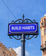 Obraz premium Build habits symbol. Concept word Build habits on beautiful blue road sign. Beautiful blue sky and buildings background. Business build habits concept. Copy space.