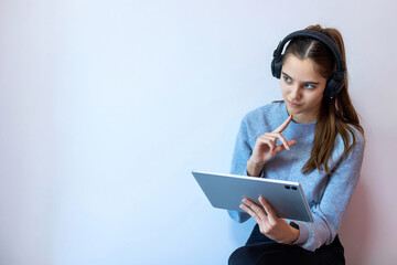 Teen girl thinking while using tablet and headphones. Teenage girl wearing headphones and holding a tablet, looking thoughtful and focused, possibly studying or watching content online.
