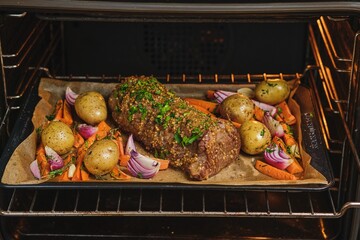 Roast beef on a baking sheet with carrots, onions, and potatoes, ready for baking in the oven. Cooking beef in the oven as a whole piece. Merry Christmas.
