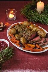 A cooked roast beef with carrots, onions, and potatoes on a white platter on a festive Christmas table setting. Merry Christmas! Beef dishes.