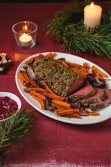 Cooked roast beef with carrots and onions on a white platter on a festive Christmas table setting. Merry Christmas! Beef dishes.