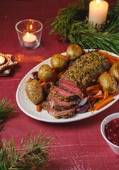Cooked roast beef with carrots and onions on a white platter on a festive Christmas table setting. Merry Christmas! Beef dishes.
