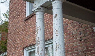 Detail of Peeling White Paint and Cracking Wood on Porch Columns of Old Red Brick House
