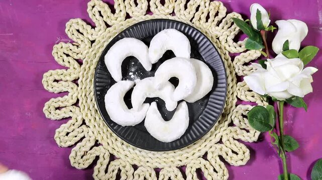 Oriental Algerian sweet cookies named tcharek aryen in arabic which mean almond cookies in english  On Black Plate With Hands, Rustic Woven Mat And White Roses 