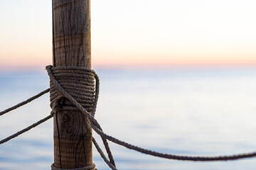 Wooden pier post with rope railing and sea horizon in the background; with copyspace