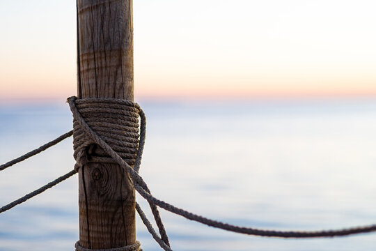 Wooden pier post with rope railing and sea horizon in the background; with copyspace