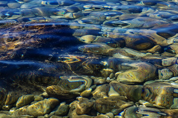 Underwater pebble stones on sea bottom in clear blue water. Natural summer background, beach seascape texture for travel and vacation images