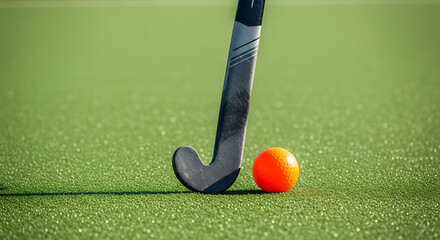 A field hockey stick and orange ball on a green field in a close up shot on a sunny day outside ai generated