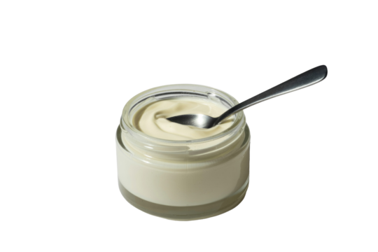 A small glass jar filled with creamy white yogurt or sauce, featuring a silver spoon dipped inside, presented on a transparent background. background removed