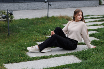 Woman relaxing on stone pathway in a garden wearing a cozy sweater and stylish pants during an...